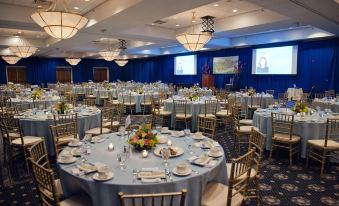 a large banquet hall filled with round tables and chairs , set up for a formal event at UMass Lowell Inn and Conference Center
