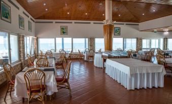 a large dining room with wooden tables and chairs , white tablecloths , and a view of the ocean at Murdeira Village Resort