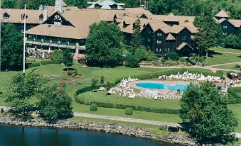 a large resort with a pool surrounded by grass , trees , and a lake in the background at Fairmont le Château Montebello