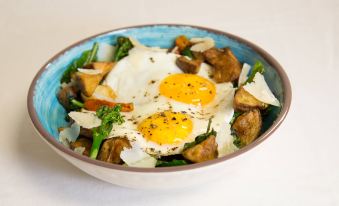 a blue and white bowl filled with mixed vegetables , including broccoli , mushrooms , and eggs , sitting on a dining table at Courtyard Redwood City