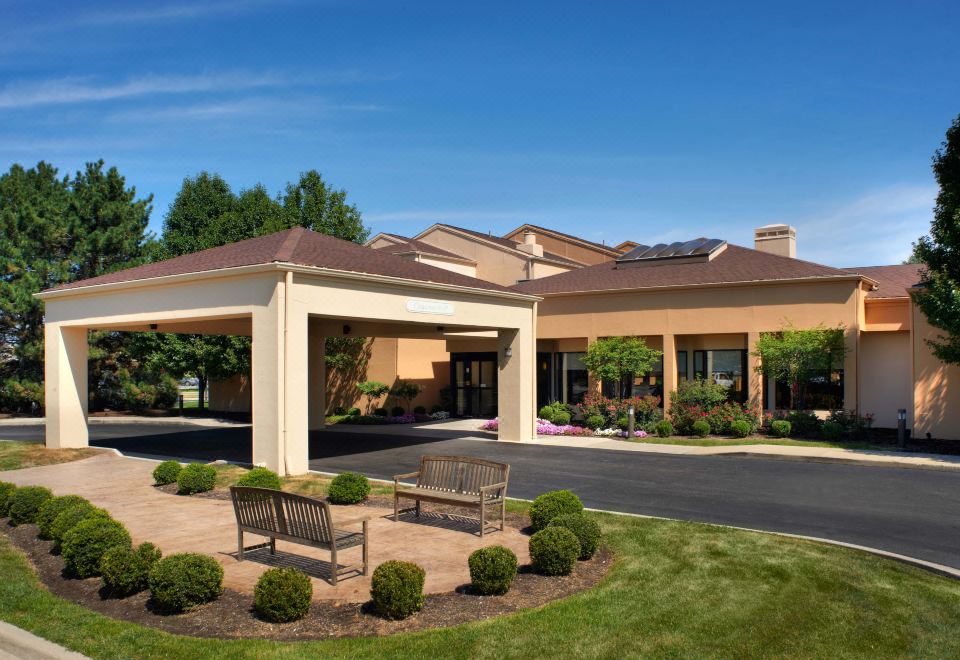 an entrance to a hotel with a parking lot and several benches in front of it at Courtyard Toledo Airport Holland