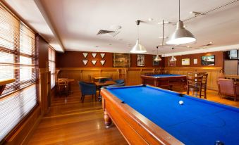 a pool table with a blue felt top and wooden cabinets in the background , surrounded by chairs at Wilsonton Hotel