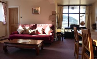 a cozy living room with a red couch , wooden table , and dining table in the background at Orchard House Bed and Breakfast