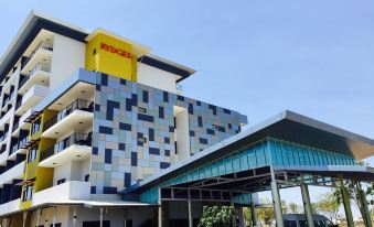 a modern hotel with a yellow sign on the front , surrounded by trees and cars at Rydges Palmerston - Darwin, an EVT hotel