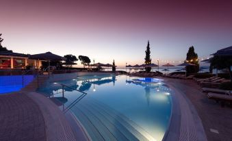 a large outdoor swimming pool surrounded by lounge chairs and umbrellas , with the sun setting in the background at Poseidon Palace