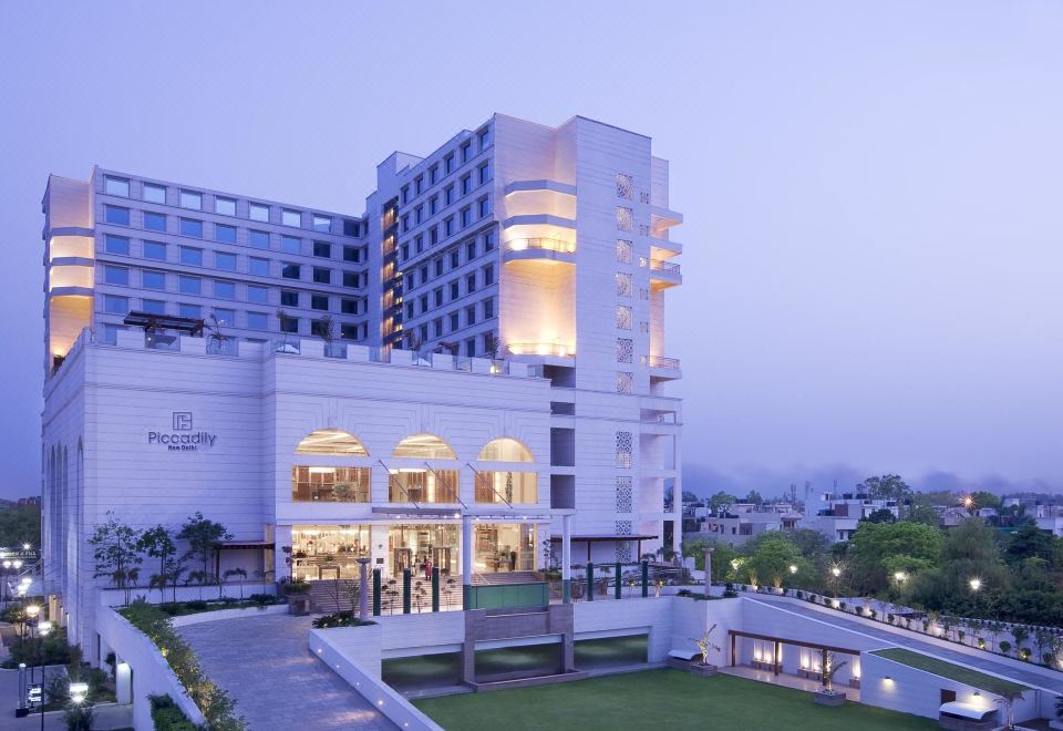 a modern hotel building with a white exterior and large windows , surrounded by a grassy area at Hyatt Centric Janakpuri New Delhi