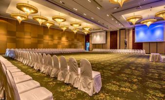 a large , well - lit conference room with rows of white chairs arranged in a symmetrical pattern , and a projector screen on the wall at Mida Resort Kanchanaburi