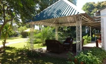 a covered outdoor area with a thatched roof , surrounded by lush greenery and trees , providing a relaxing outdoor space at Fawlty Towers Guest House