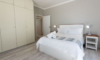 a white bedroom with a large bed , a closet , and a door leading to a bathroom at De Nada