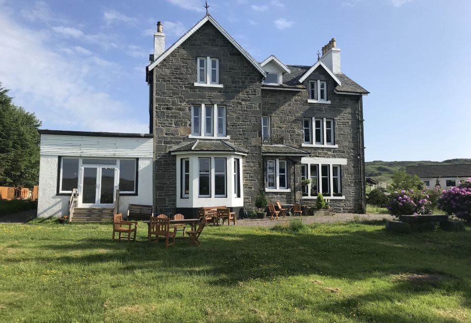 a large stone house surrounded by a lush green lawn , with several benches placed in front of it at Loch Shiel Hotel