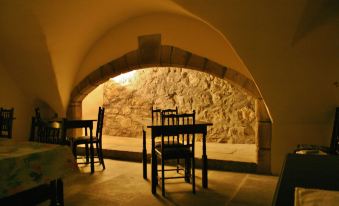 a room with wooden chairs and tables , a stone wall in the background , and sunlight streaming through a arched window at Leslie Castle