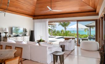 a modern living room with a large window and sliding glass door leading to an outdoor patio , overlooking the ocean at Como Parrot Cay