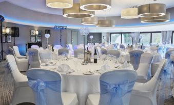 a large dining room with white chairs and tables set up for a wedding or special event at Leonardo Hotel and Conference Venue Hinckley Island