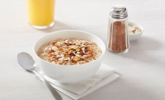 a white bowl filled with oatmeal sits on a dining table , accompanied by a cup of orange juice at Residence Inn Hartford Windsor