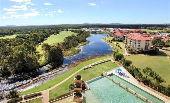 a man sitting on a balcony overlooking a swimming pool , surrounded by lush greenery and a golf course at Pelican Waters Resort