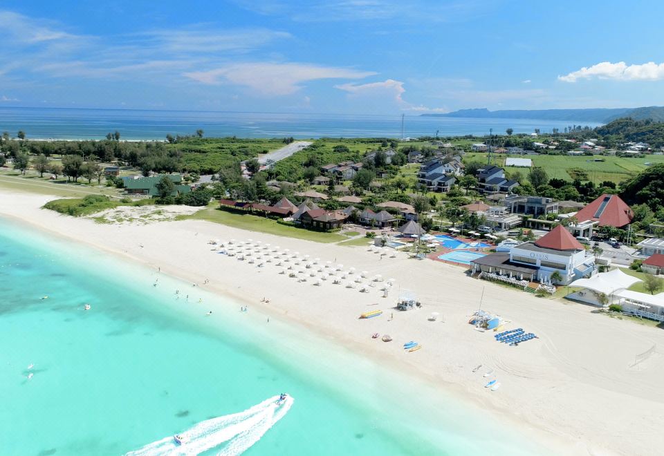 aerial view of a sandy beach with a boat in the distance and a town on the beach at Okuma Private Beach & Resort