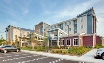 a modern building with multiple floors , surrounded by trees and flowers , under a clear blue sky at Residence Inn Kingston