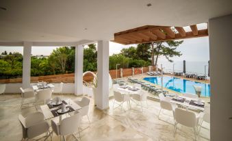 a restaurant with white tables and chairs is situated next to a pool and overlooking the ocean at Poseidon Hotel