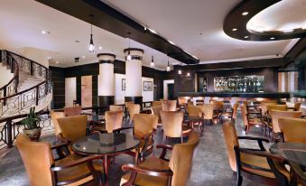 a modern restaurant with wooden chairs and tables , black pendant lights , and a bar area at Aston Karimun City Hotel