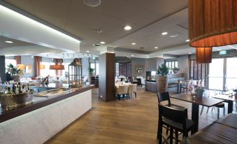 a large , well - lit dining area with wooden floors and a long buffet table filled with various food items at Leonardo Hotel Papendrecht