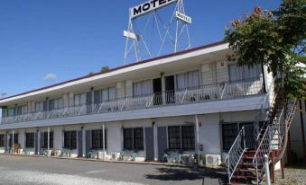 a motel with a large sign on the roof , surrounded by trees and parked cars at Monto Colonial Motor Inn