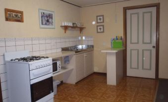 a kitchen with white appliances , wooden floors , and tile walls , including a stove top oven and sink at Fernleigh Accommodation