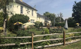 a large white building with a wooden fence in front of it , surrounded by green grass and trees at The Mortimer Arms