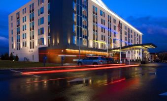 a modern hotel building with blue lights and a red car driving by in the evening at Aloft Mount Laurel