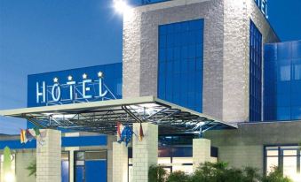 "a modern hotel building with the name "" garda hotel "" prominently displayed on its facade , illuminated by lights against a blue sky" at Garda Hotel