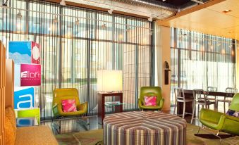 a modern living room with colorful chairs , a large round coffee table , and a window at Aloft Chesapeake