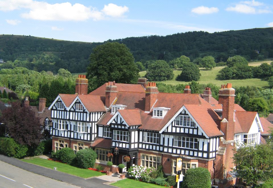 a large , tudor - style building with red roof tiles and blue trim , situated in a rural setting surrounded by greenery at Colwall Park - Hotel, Bar & Restaurant