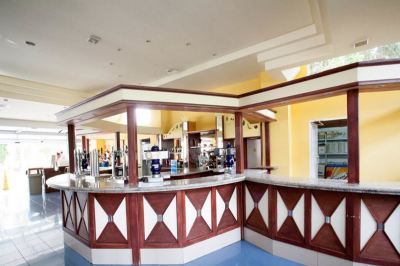 a bar area with a long wooden counter , several bottles of beer , and a cup on the counter at Club Mac Club Mac - All Inclusive Family Resort Photo