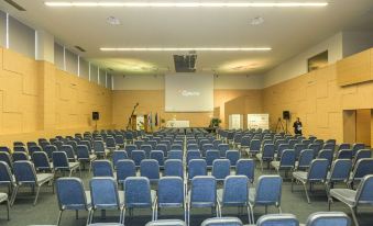 a large conference room with rows of blue chairs arranged in a semicircle , and a projector mounted on the wall at Hotel Olympia