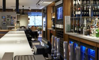 a modern bar with a large window , wooden shelves filled with wine bottles and glasses , and a sleek white counter at Holiday Inn London - Brentford Lock