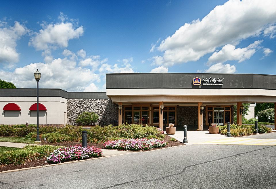 a large building with a red sign on the front , surrounded by bushes and flowers at SureStay Plus Hotel by Best Western Lehigh Valley