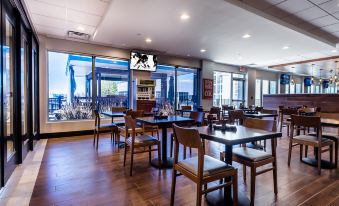 a restaurant with wooden tables and chairs , a large window , and a television mounted on the wall at Holiday Inn Grand Haven - Muskegon