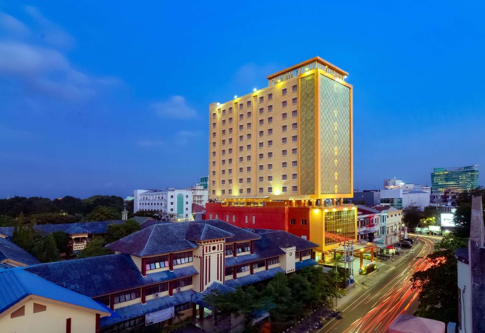 a tall building with many windows is surrounded by a modern cityscape at night , with buildings lit up in various colors at Best Western Plus Makassar Beach
