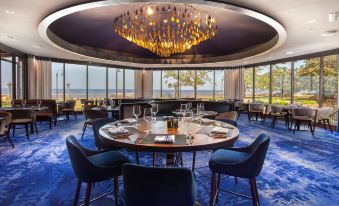 a restaurant with blue carpet and a large chandelier hanging from the ceiling , creating an elegant atmosphere at The Grand Hotel Golf Resort & Spa, Autograph Collection