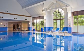 an indoor swimming pool with blue water , surrounded by lounge chairs and a wooden ceiling at Holiday Inn Glasgow - East Kilbride