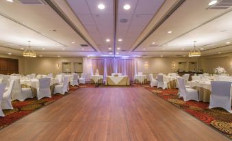 a large , empty banquet hall with wooden floors and white tables set up for a formal event at Hotel Mtk Mount Kisco