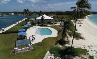 aerial view of a resort with a swimming pool surrounded by grass , palm trees , and a body of water at Cape Eleuthera Resort & Marina