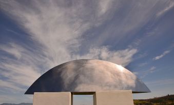 a large , arched metal structure against a cloudy blue sky , with two white panels in front of it at Casa de la Piedra