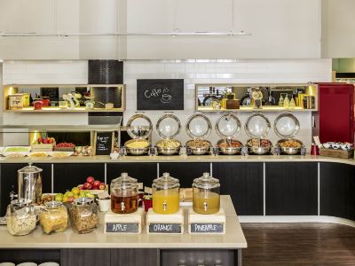 a kitchen with a variety of food items and drinks on display , including fruits , nuts , and beverages at Ibis Melbourne Hotel and Apartments