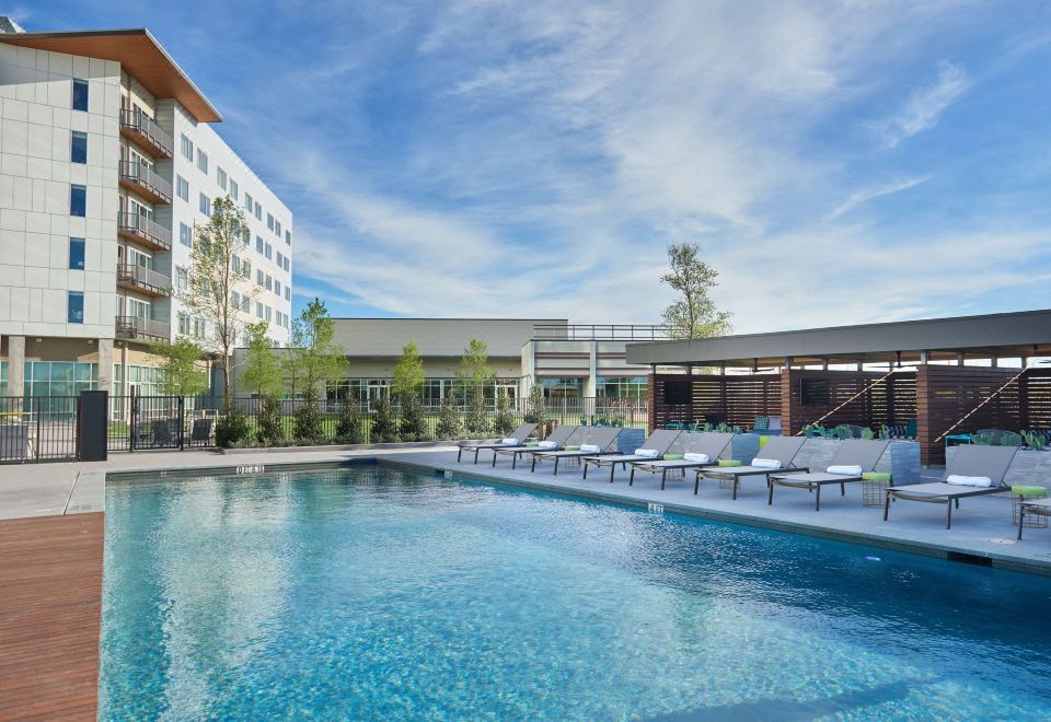 a large swimming pool surrounded by lounge chairs and umbrellas , with a building in the background at The Stella Hotel, Autograph Collection