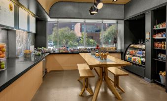 a modern kitchen with a wooden table and stools , a refrigerator , and a window overlooking a street at Aloft Chapel Hill