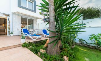 a tropical outdoor setting with blue lounge chairs , palm trees , and greenery surrounding a white building at Golf