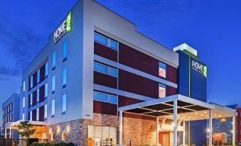 an exterior view of a hotel building at night , with a large sign above the entrance at Home2 Suites by Hilton Gonzales