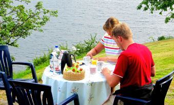 a man and a woman are sitting at a table with food and drinks , near the water at Juv