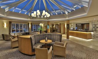 a modern hotel lobby with a glass ceiling , wooden furniture , and a wine bottle on the counter at Manor House Hotel & Spa, Alsager