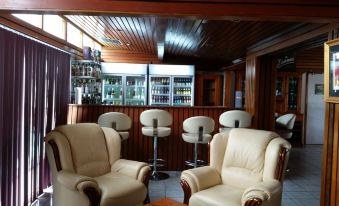 a room with a wooden ceiling and floor , featuring two white armchairs and a bar with stools at Ambassador Motel